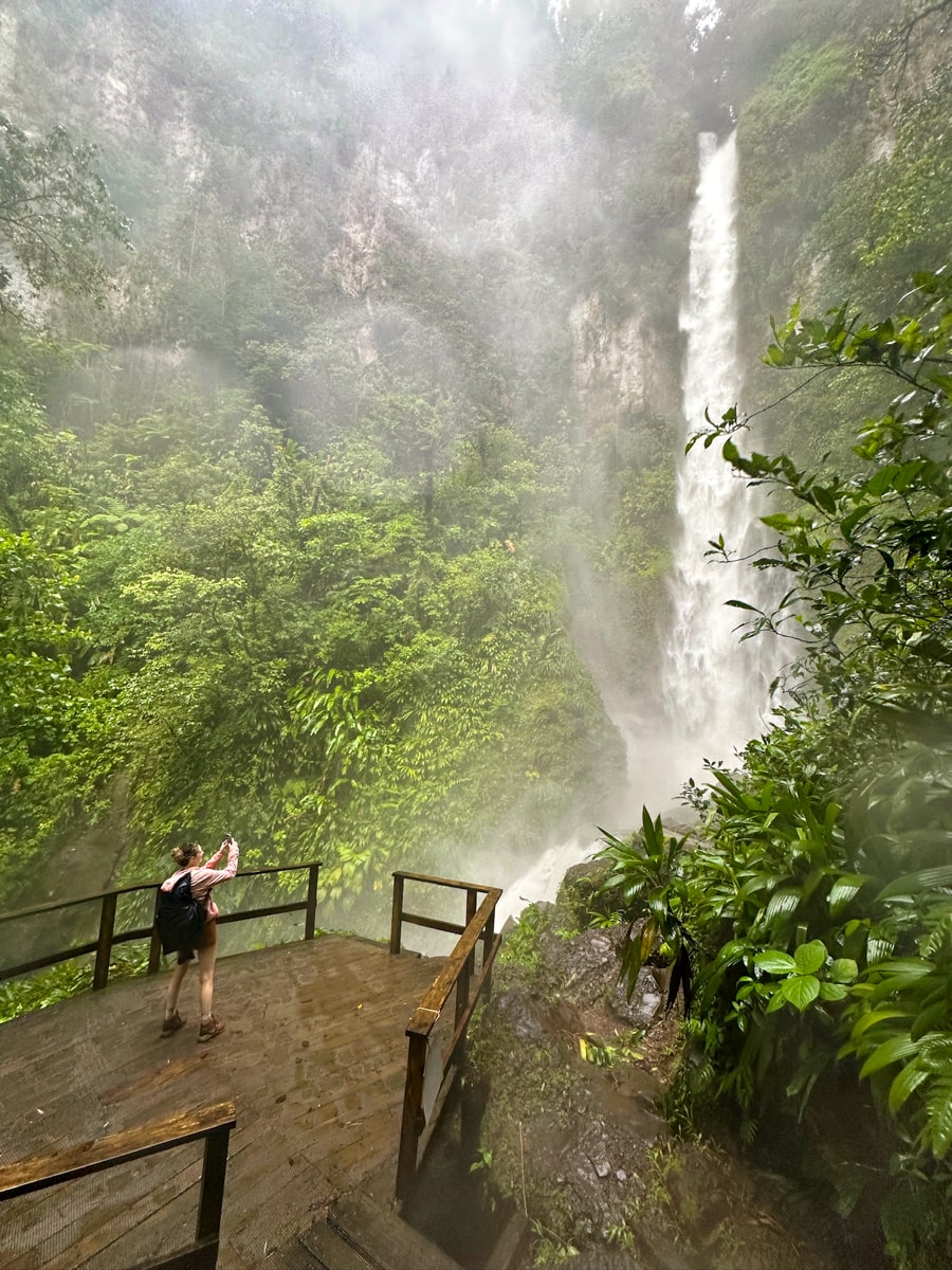 woman trying to take a photo of Middleham Falls from the viewing platform but is getting covered in mist