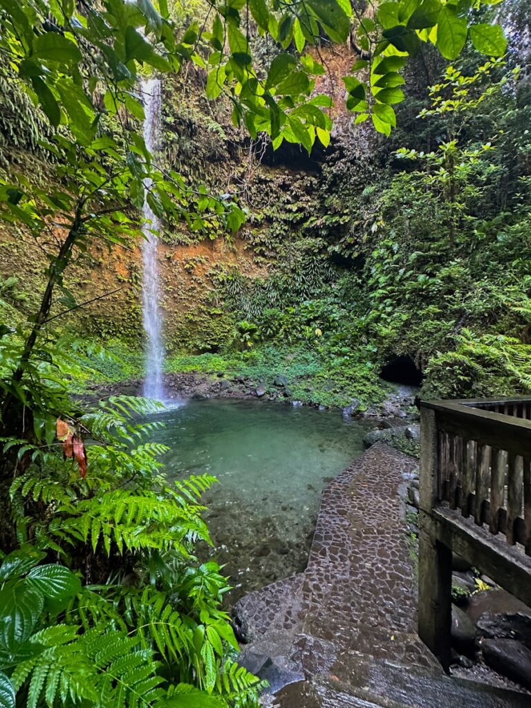 paved pathway in front of Spanny Falls waterfall with blue swimming hole in Dominica, Caribbean.
