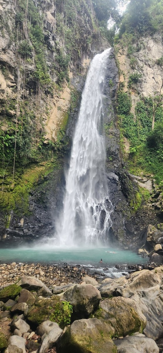 Person standing in the milky-blue swimming hole at the base of Victoria Falls surrounded by rocks