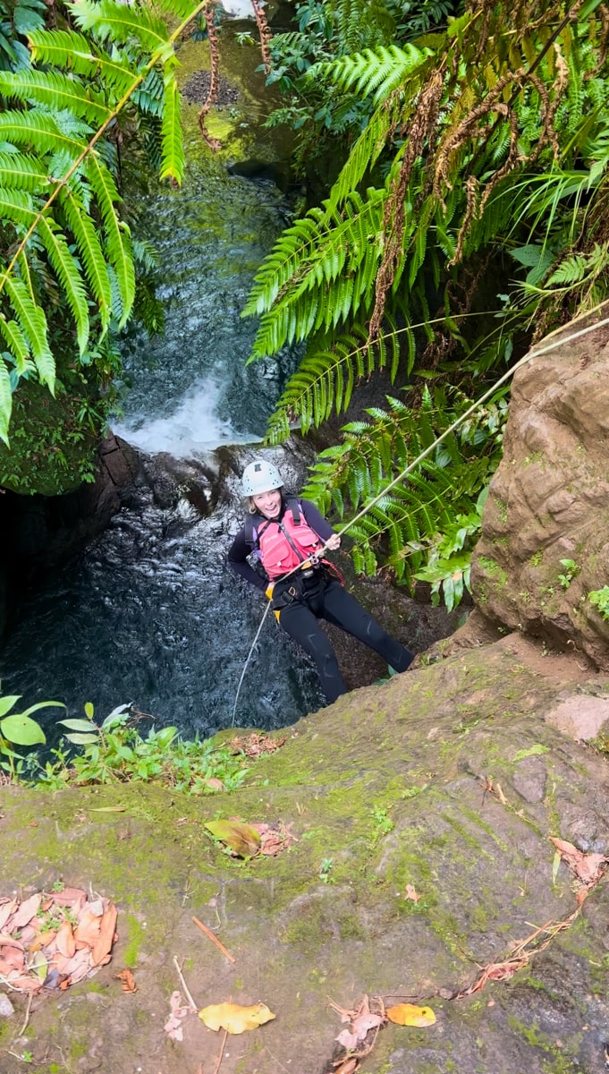 woman rappelling down a cliff into the canyon below in dominica