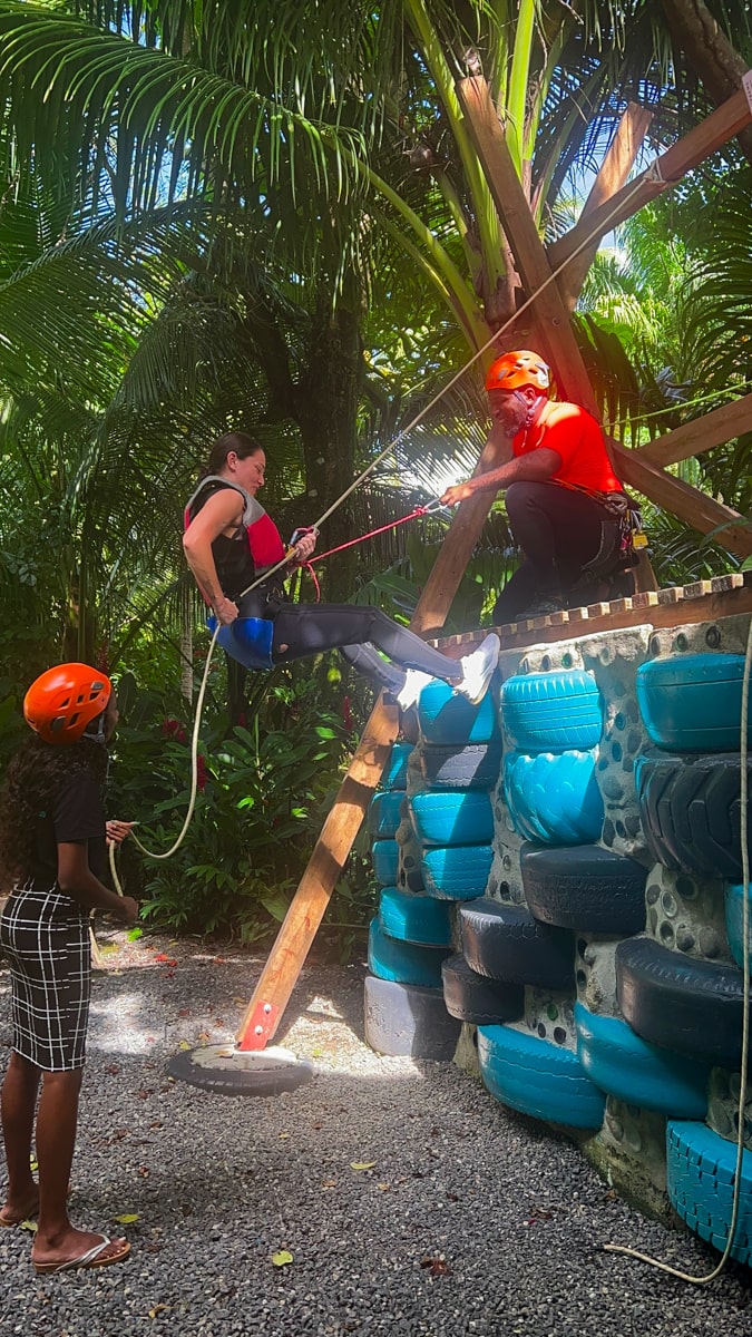 woman practicing rappelling down a makeshift wall with tour guides in Dominica
