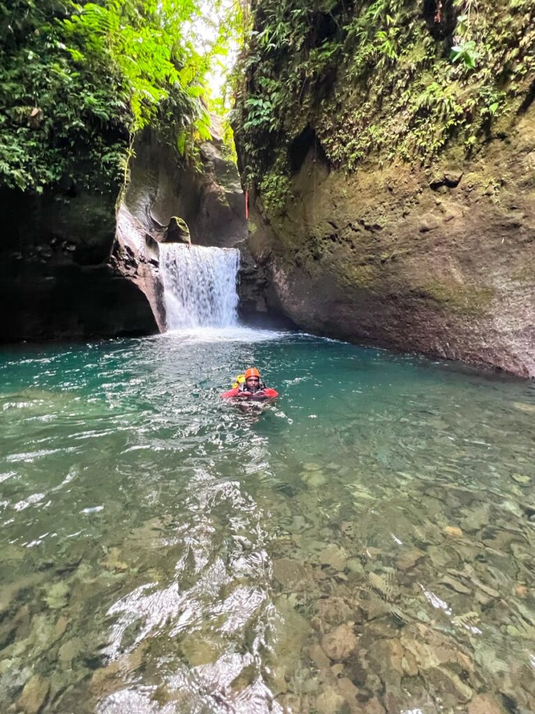 person swimming in titou gorge in front of a waterfall on a canyoning tour in Dominica