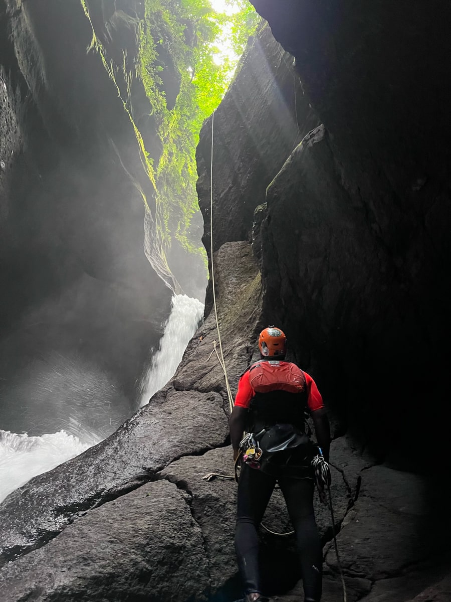 tour guide holding a rappelling line at the bottom of a large rock beside a waterfall waiting for a person to rappel down the rock