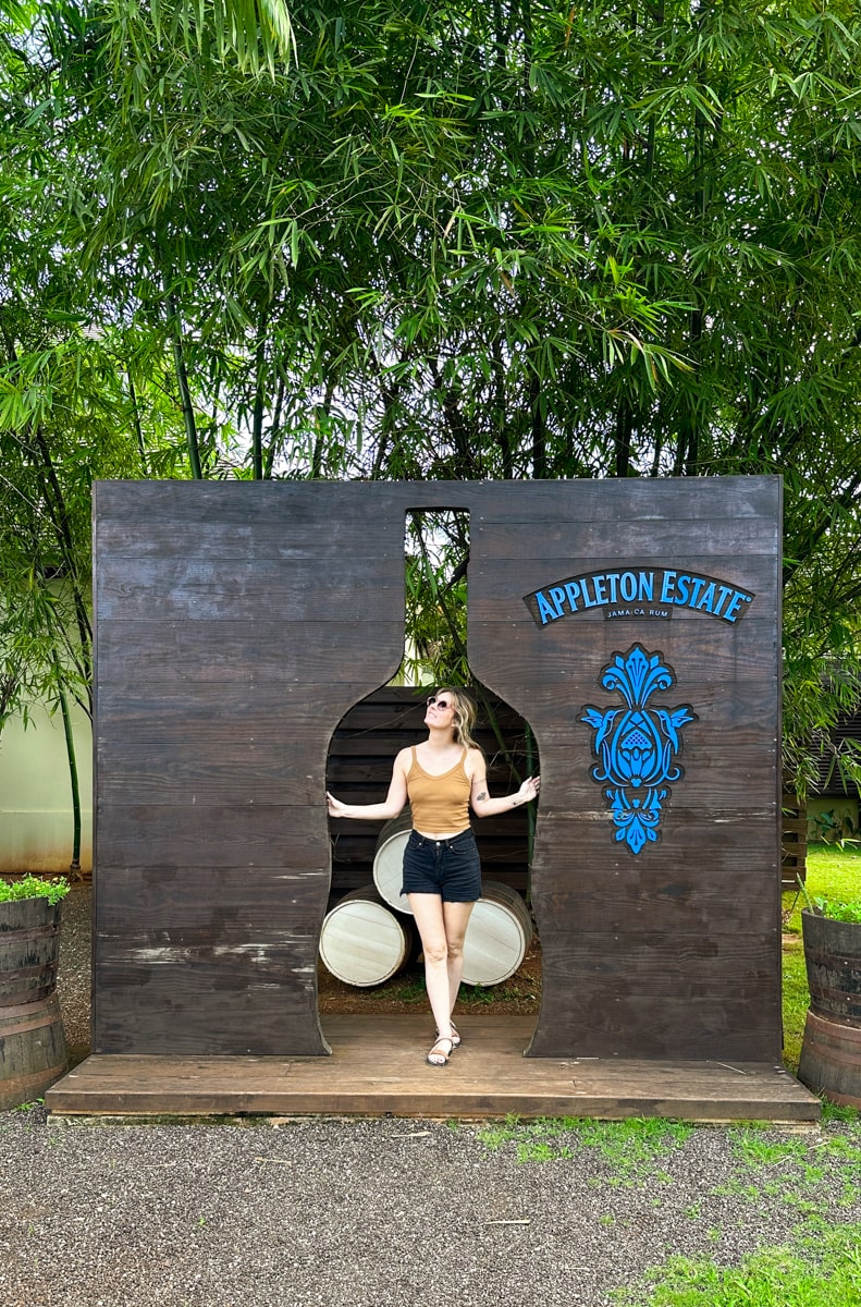 woman standing in front of bottle shaped Appleton Estate sign going on a rum tasting tour in jamaica