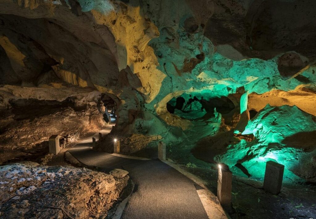 inside green grotto caves with limestone formations lit up by green light and a pathway, a unique thing to do in jamaica