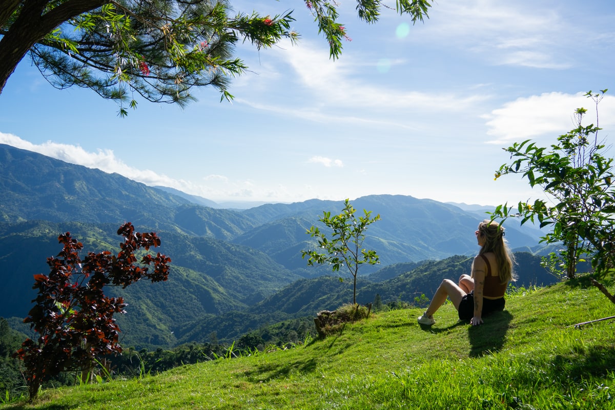woman sitting on the grass overlooking the Blue Mountains in Jamaica on a sunny day