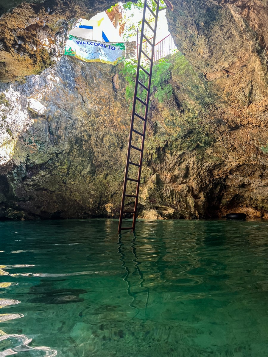 view of the Blue Hole mineral springs from inside floating in the blue water with the sun shining through the hole above 