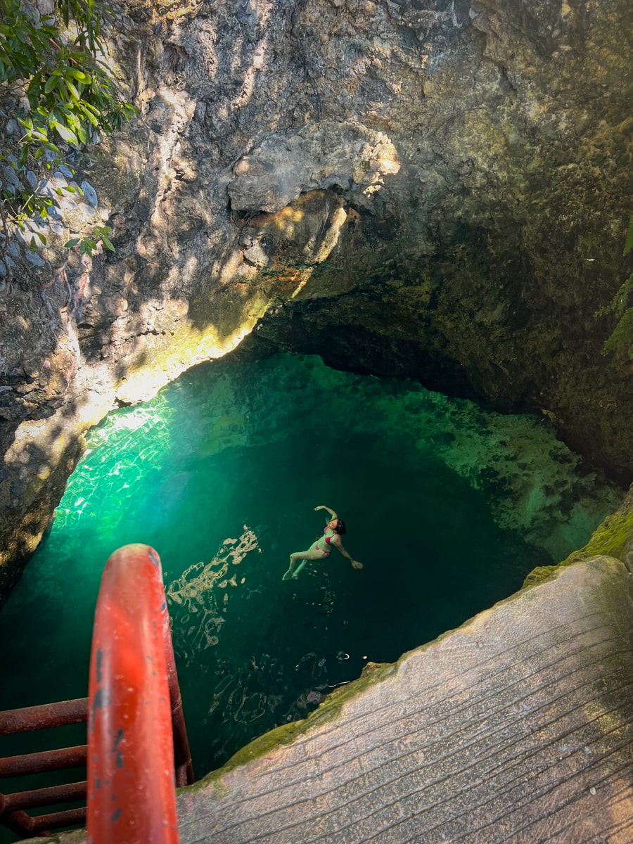 woman floating in a cenote water-filled limestone cavern with blue water and a red ladder
