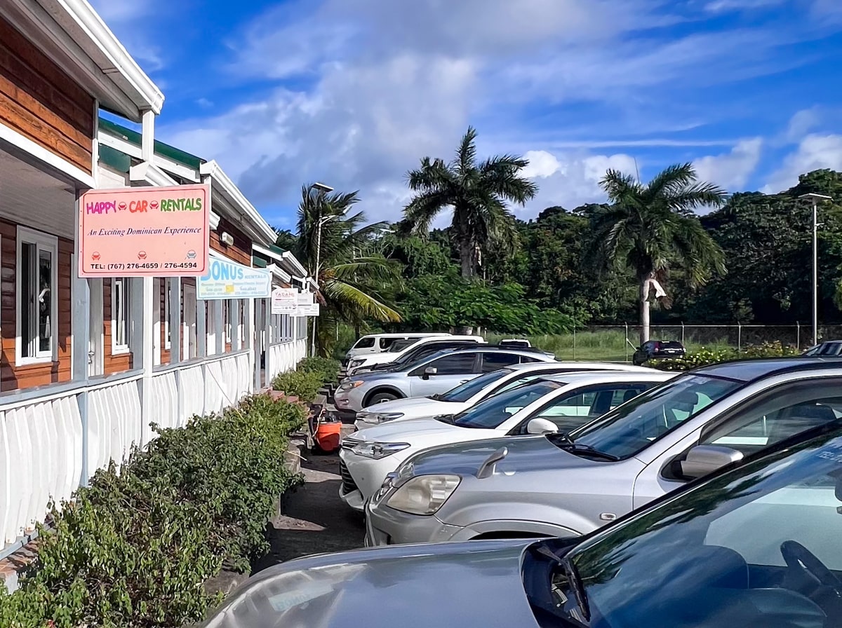 sign for happy car rentals in Dominica with parked rental cars out front