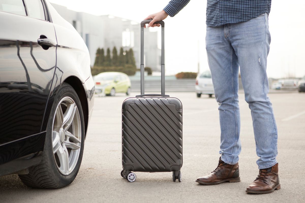 person standing by a rental car with rolling luggage