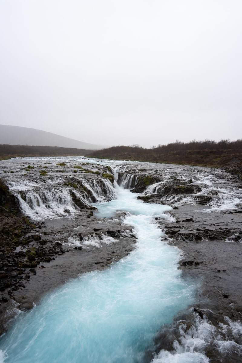 Popular blue river and waterfall in Iceland called the Bruarfoss with gray skies