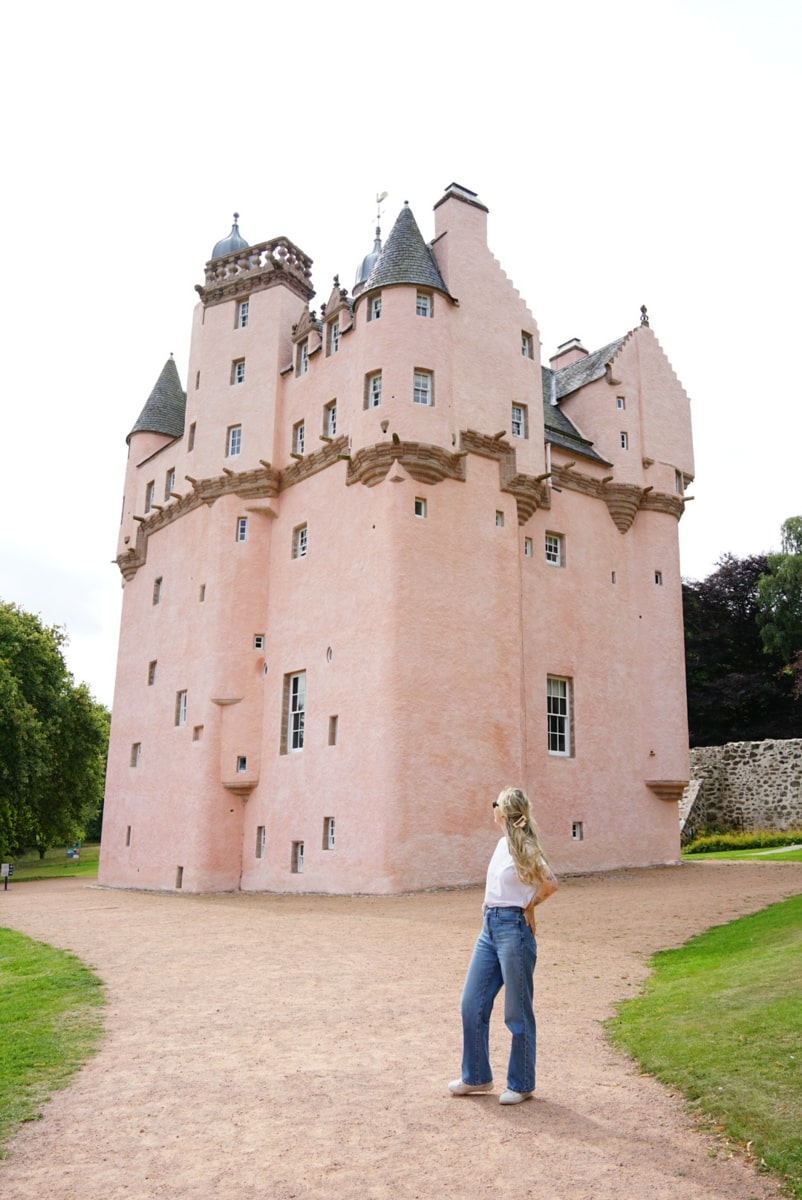 Woman standing in front of a pink castle in Scotland called Craigievar Castle