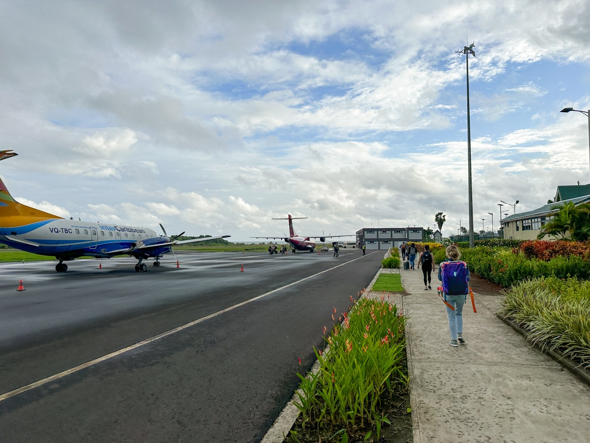 person with a Cotopaxi backpack walking along the pathway to the small plane on the runway at the airport in Dominca