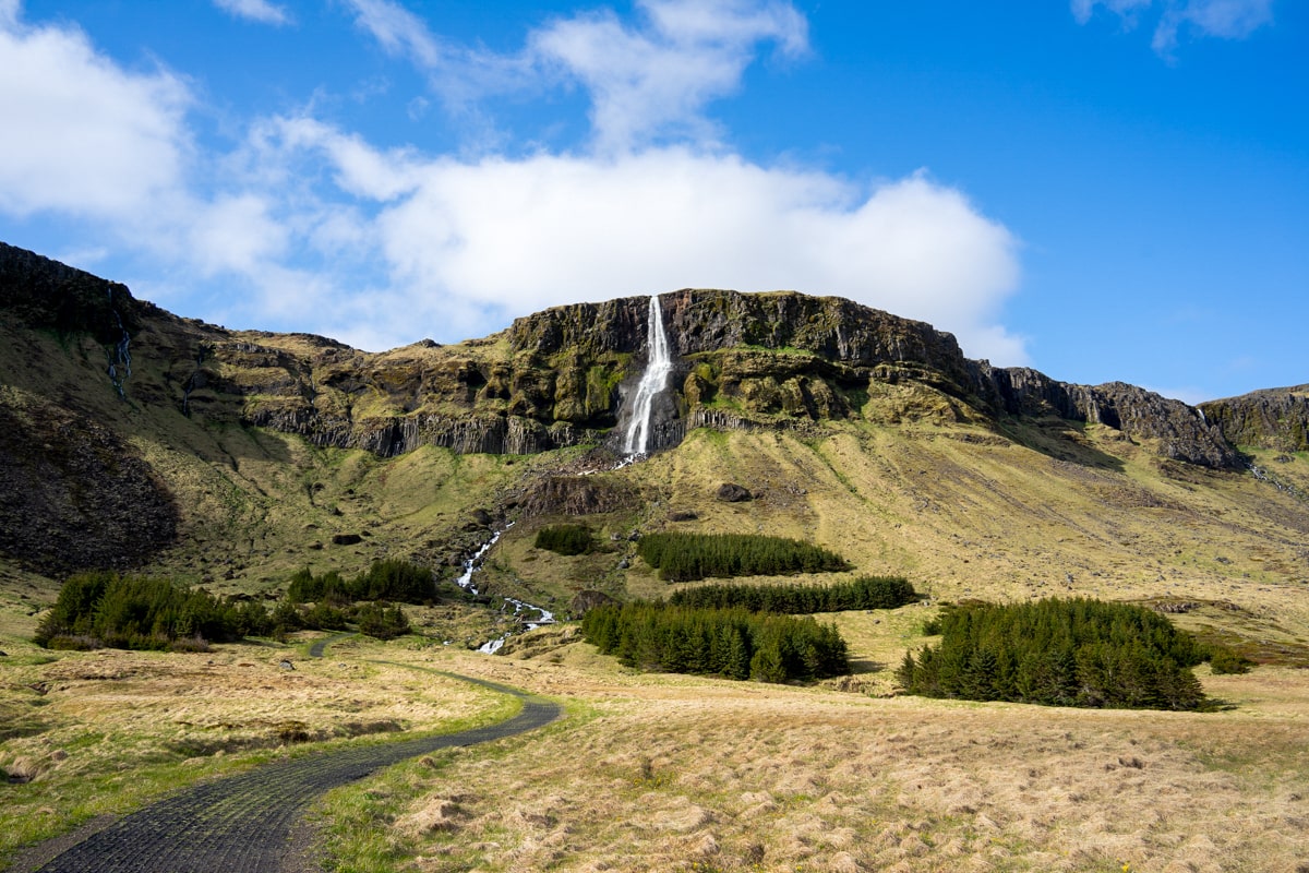 view of Bjarnarfoss Waterfall along the Snaefellsnes Peninsula with blue skies and white puffy clouds