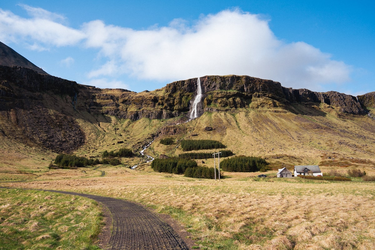 view of Bjarnarfoss waterfall from the pathway with blue skies and clouds