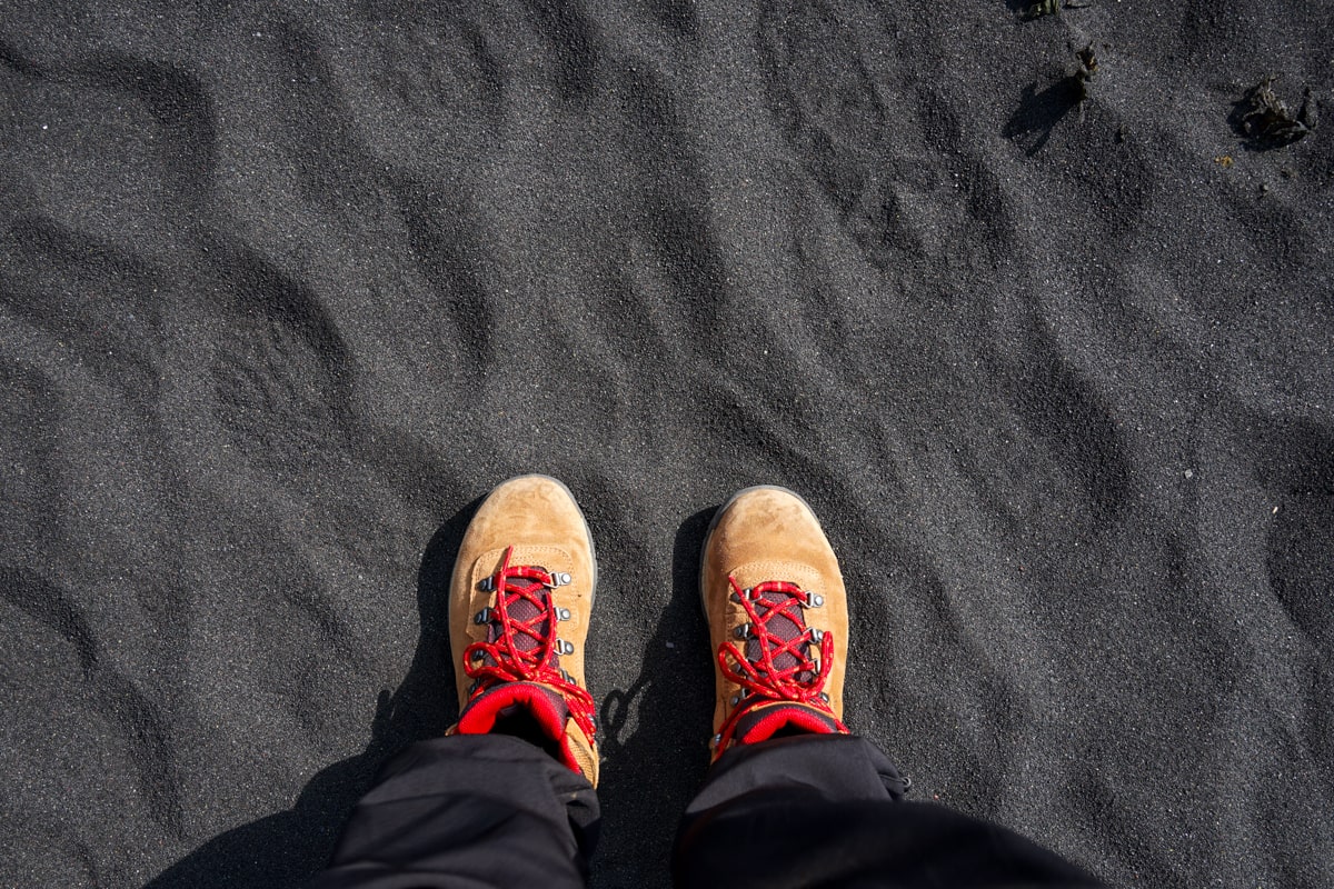 standing on a black sand beach in iceland with contrasting columbia hiking boots with red laces
