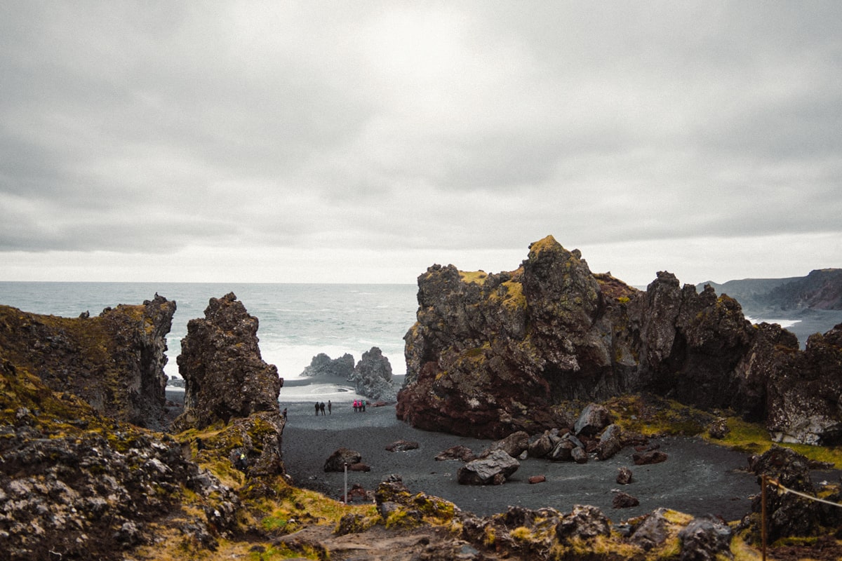 People walking along Djupalonssandur beach in between large rock formations on the Snaefellsnes Peninsula in Iceland