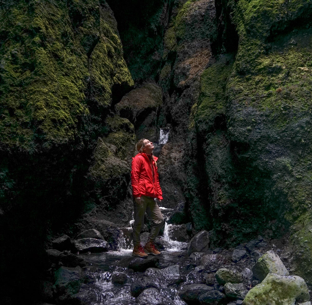woman standing inside Raudfeldsgja Gorge looking up at the sky in a red jacket
