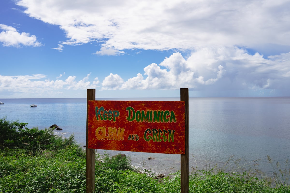 A "Keep Dominica Clean and Green" sign sitting in front of the blue ocean