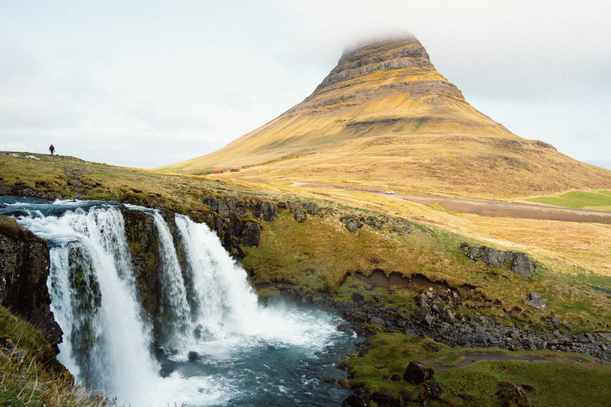 person walking along path in front of Kirkjufell Mountain and waterfall
