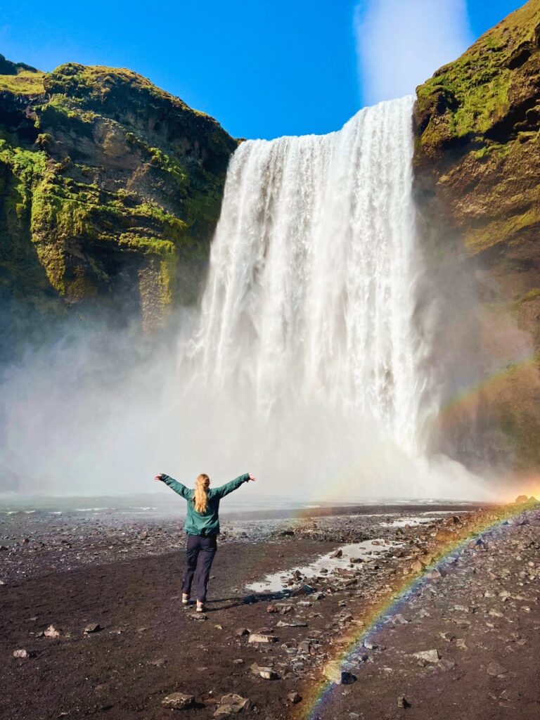 woman standing in front of Skógafoss watefall in Iceland with a rainbow