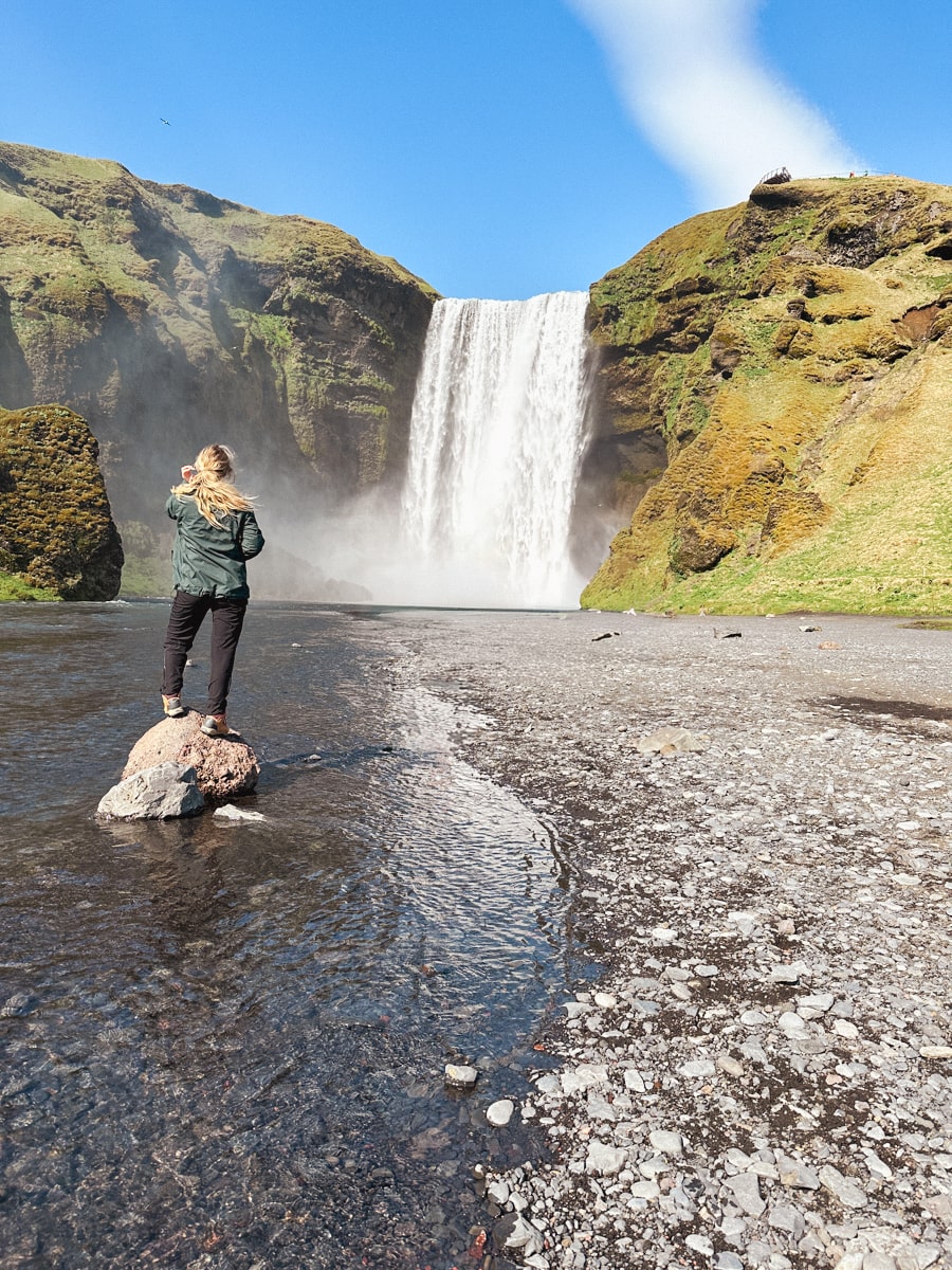 woman standing on rock in the water in front of Skogofoss waterfall in Iceland