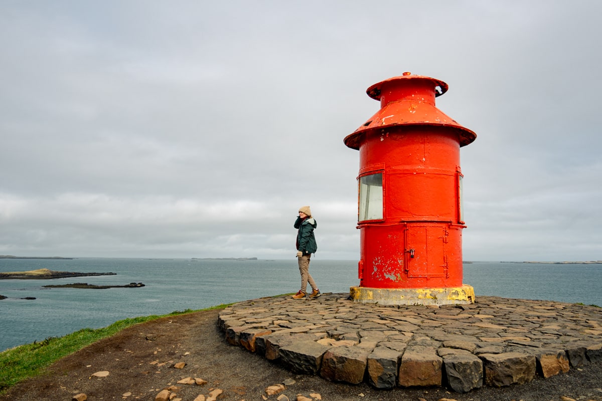 Woman standing at the orange colored Súgandisey Island lighthouse overlooking the ocean in Iceland