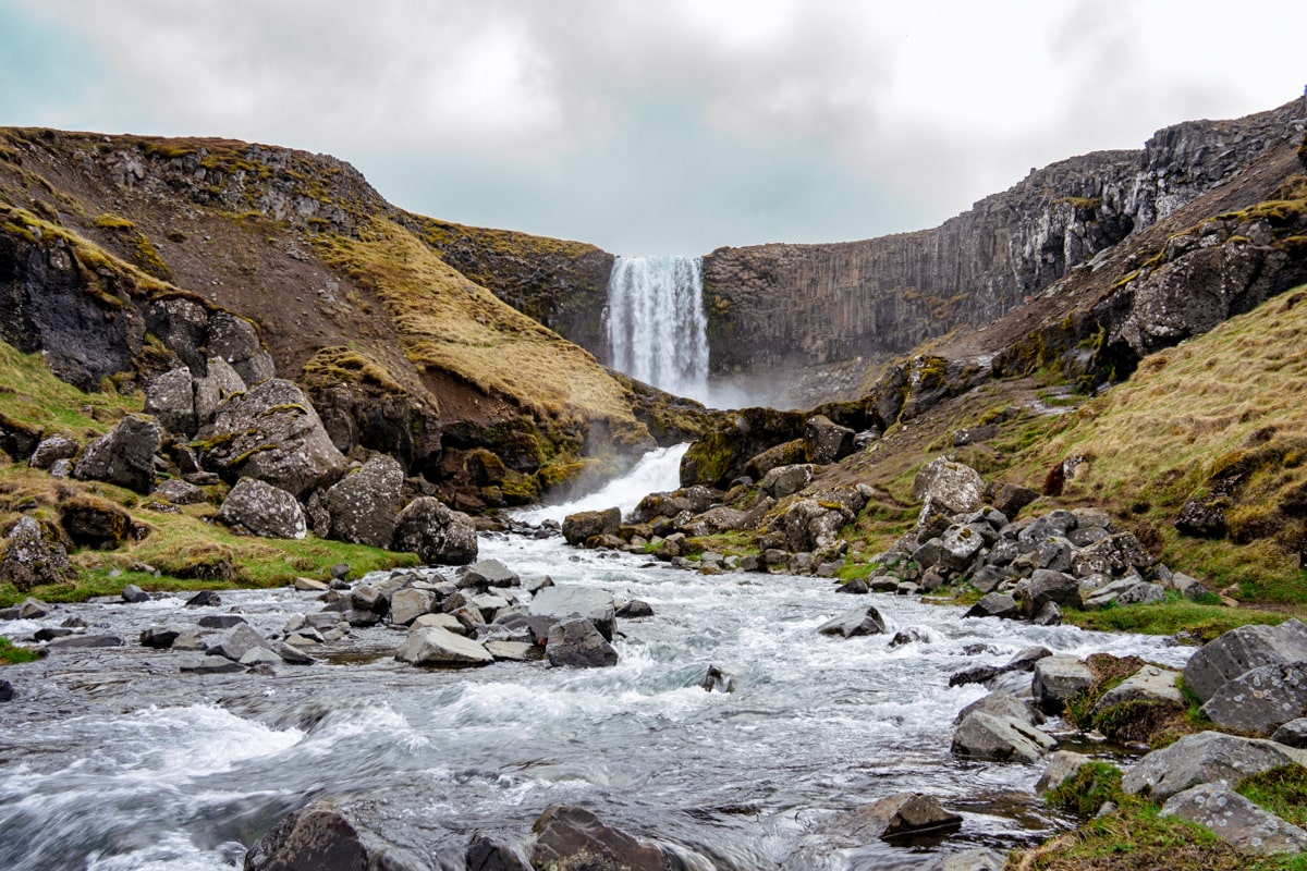 view of Svodufoss waterfall from down river on a cloudy day surrounded by rocks and moss