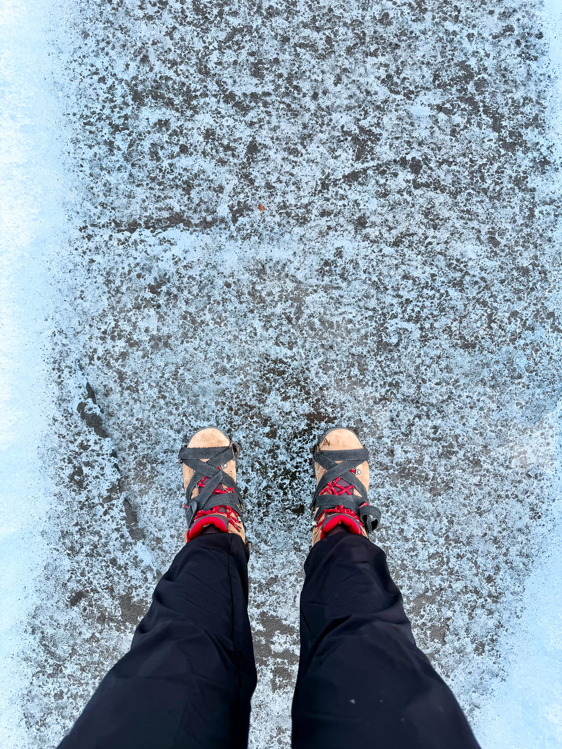 Person looking down at their feet on the Perito Moreno Glacier with boots and crampons on the blue ice
