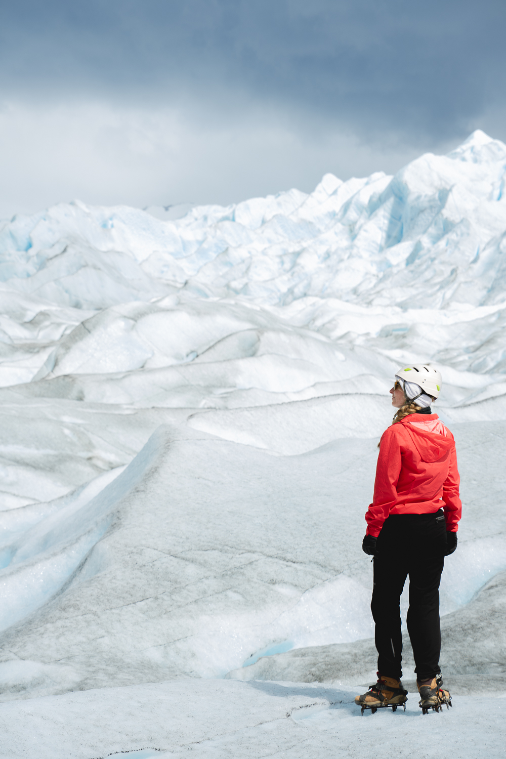Person standing on the Perito Moreno glacier with a red jacket and crampons on boots
